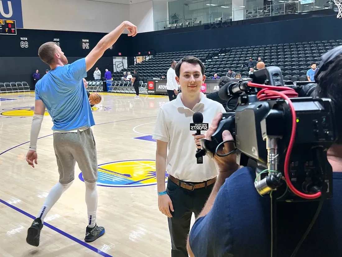 Luke Backman sideline reporting at a basketball game inside of a gym.